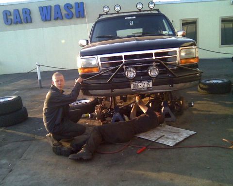1995 Ford Bronco - Two men work on the front suspension of a 1995 Ford Bronco, which is raised on jack stands.