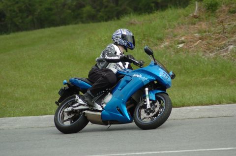 2007 Kawasaki Ninja R - A rider on a blue Kawasaki Ninja motorcycle is seen from the front-three-quarter angle on a paved road with a grassy hill in the background.