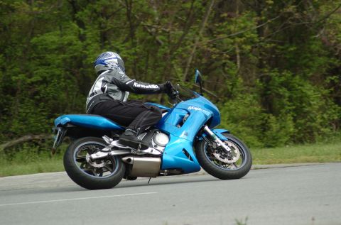2007 Kawasaki Ninja R - A rider on a blue 2007 Kawasaki Ninja R motorcycle cruises down a road with trees in the background.