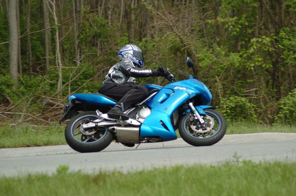 Rider leaning a blue Kawasaki Ninja sport bike through a curve on a wooded road