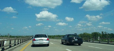 2001 Ford Crown Victoria - Two sedans drive on a highway on a clear day with scattered clouds.