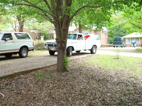 1977 Ford F-100 - A white 1977 Ford F-100 pickup truck with a camper shell is parked in a driveway, with other vehicles visible.