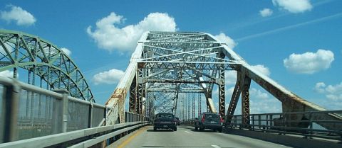2001 Ford Crown Victoria - Two vehicles traverse a large, weathered metal truss bridge under a bright blue sky with scattered clouds.