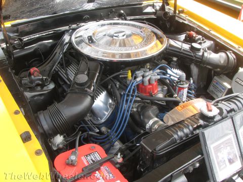 1968 Ford Mustang - The engine bay of a yellow 1968 Ford Mustang is visible, a chrome air cleaner and a red battery.