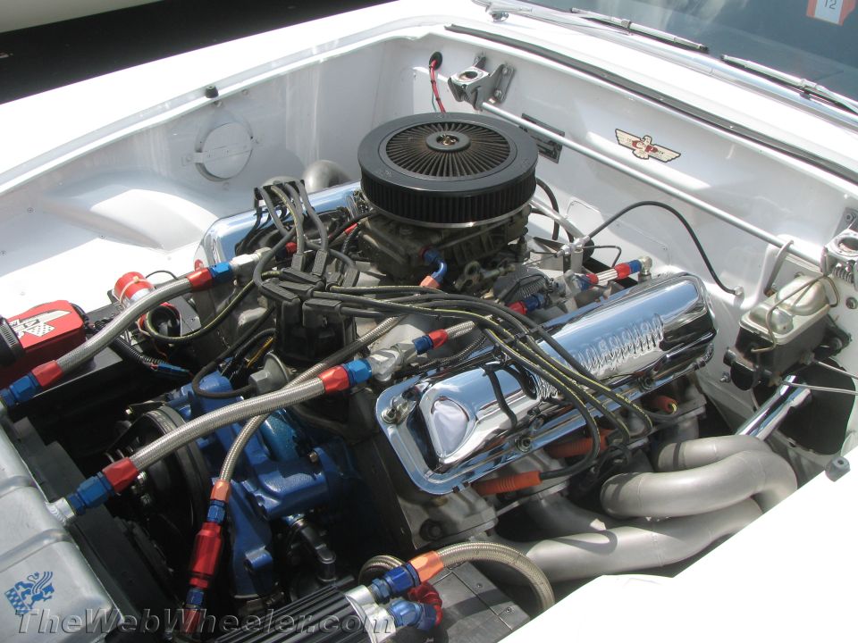 White car engine bay with chrome valve covers, black air filter, and blue and red braided hoses
