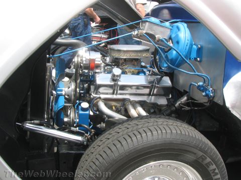 1968 Ford Mustang - Close-up of a V8 engine bay, chrome components and blue detailing, with a tire in the foreground.