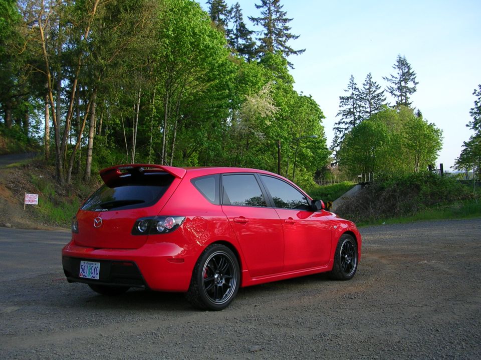 Red 2007 Mazda 3 hatchback parked on a gravel road with trees in the background