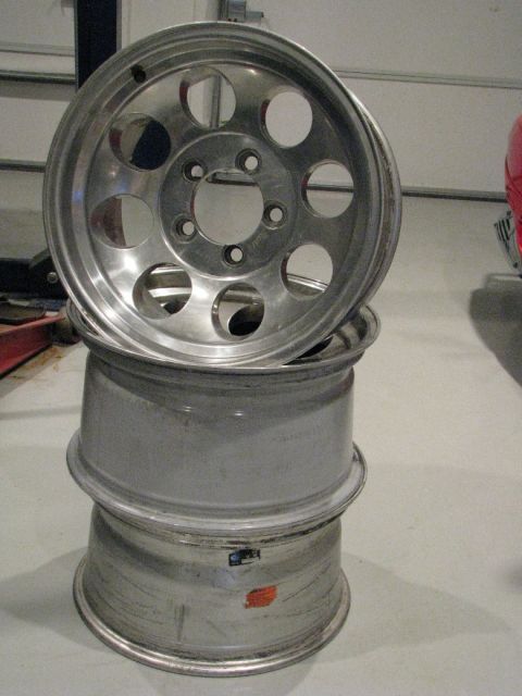 2008 Ford Bronco - Three aluminum wheels stacked up, one with a hole pattern visible.