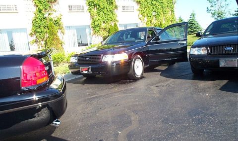 2001 Ford Crown Victoria - A black 2001 Ford Crown Victoria is parked with its driver's door open, alongside another similar vehicle.
