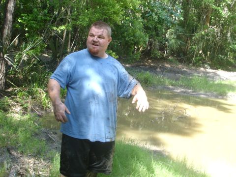 1989 Ford Bronco - Man in muddy clothes stands near a muddy puddle in a wooded area with a SUPERMOTORS.NET watermark.