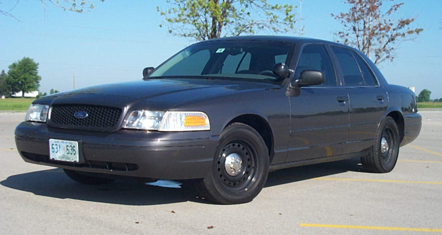 Grey Ford Crown Victoria Police Interceptor with headlights on in an empty parking lot