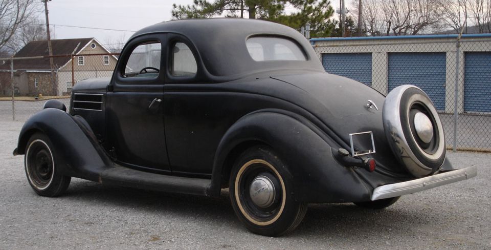 Matte black 1930s Ford coupe, rear three-quarter view with rear-mounted spare tire