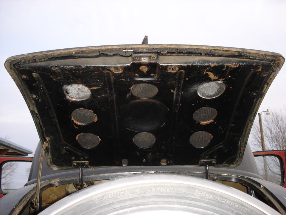 Underside of open black trunk lid with round holes over a chrome spare tire cover