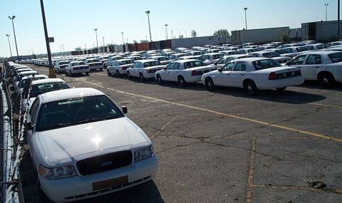 2001 Ford Crown Victoria - A fleet of white 2001 Ford Crown Victoria sedans are parked in a large lot under a clear sky.