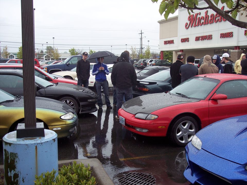 Several cars parked in a wet lot in front of a Michaels store.