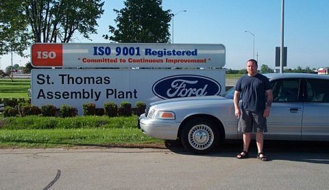 2001 Ford Crown Victoria - A silver Ford Crown Victoria sedan parked in front of the St. Thomas Assembly Plant entrance sign, which carries a blue Ford oval and an IS…