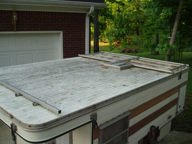 Pop-up camper roof with metal rack assembly, parked in front of a brick garage.