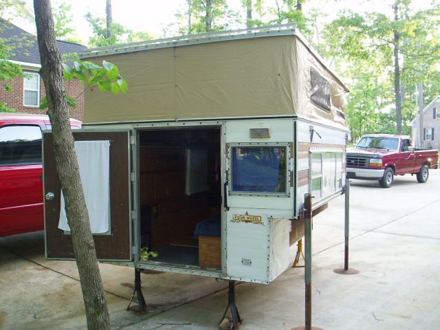 Pop-up truck camper with doors open next to a red Ford pickup truck.