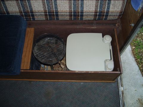 1980 Ford Bronco - Interior view of a storage compartment in a vehicle, showing a portable toilet and a small grill. A blue cushion and plaid upholstery are a…