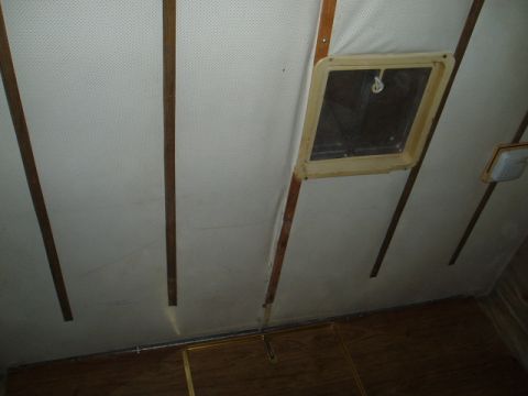 1980 Ford Bronco - The interior ceiling of a vehicle, likely an RV or camper, shows a white perforated headliner with wooden trim strips. A square vent with a…