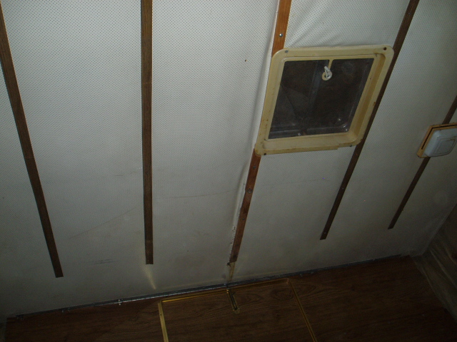 Interior ceiling of a vehicle with a white headliner, wood trim, and a ceiling vent.