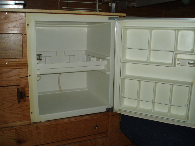 Interior of an open, empty RV refrigerator with wooden cabinetry around it