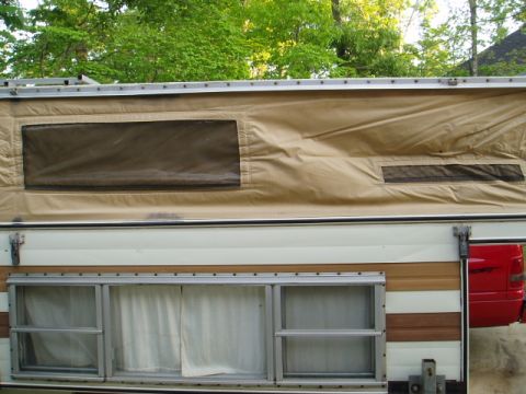 1980 Ford Bronco - A close-up view of the side of a pop-up camper, showing tan canvas with two screened windows and a section of the camper's exterior with ho…
