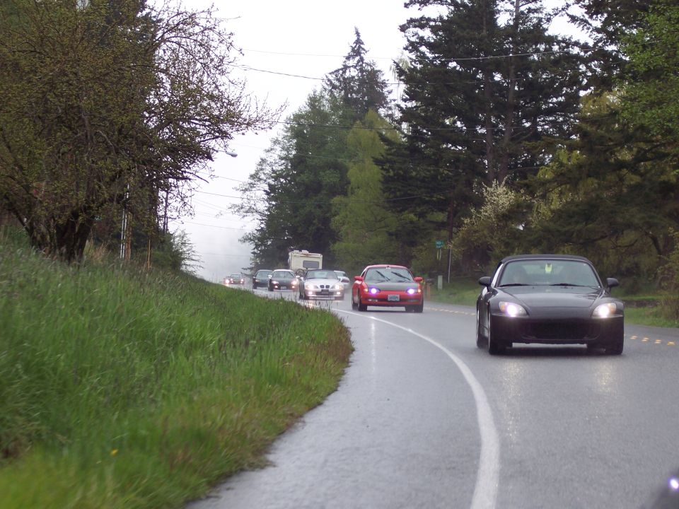 Black convertible sports car driving on a wet road.