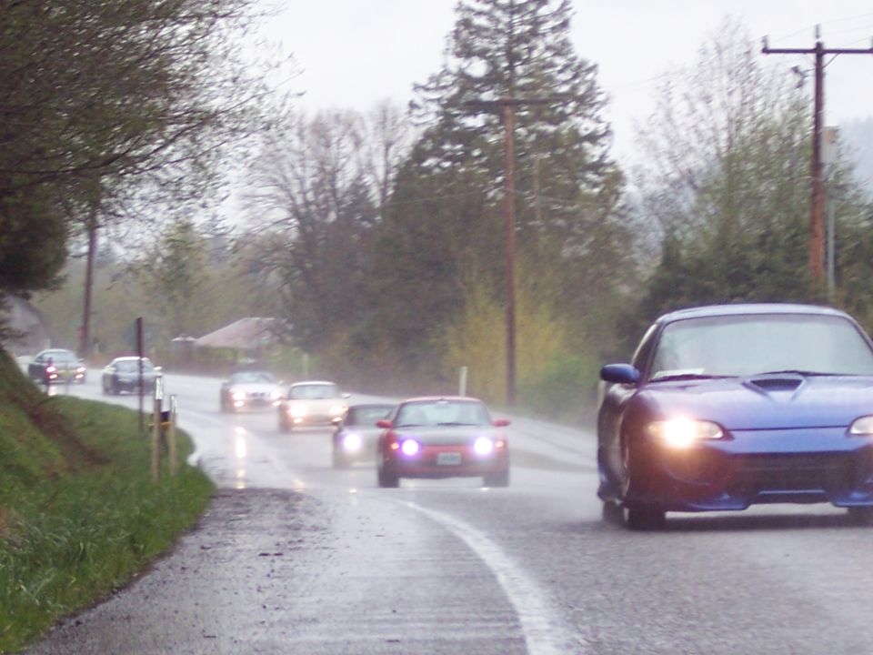 Blue sports car driving on a wet road with other cars.