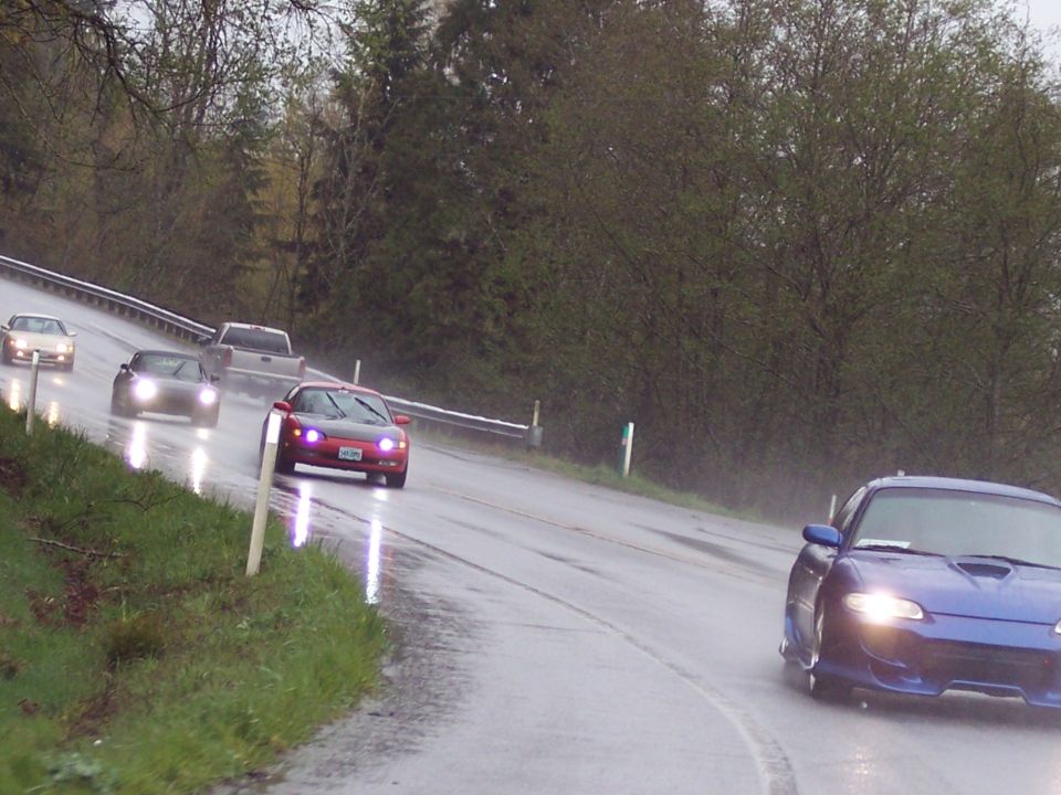 Blue sports coupe driving on a wet road in the rain.