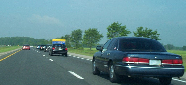 Dark blue 2001 Ford Crown Victoria on highway, rear view. Other cars visible ahead