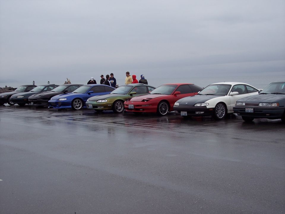 Several sports cars parked in a line on a wet road.