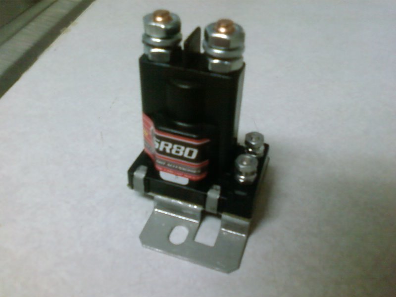A black automotive relay or solenoid on a metal mounting bracket