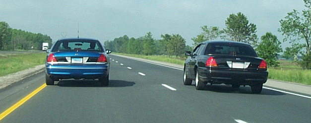 Rear view of blue and black 2001 Ford Crown Victorias on highway