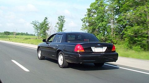 2001 Ford Crown Victoria - A black 2001 Ford Crown Victoria travels down a highway on a partly cloudy day.