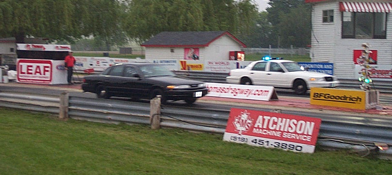 Black and white sedans on a drag strip, one with flashing lights