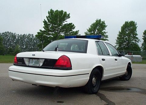 2001 Ford Crown Victoria - A white 2001 Ford Crown Victoria police car is viewed from the rear, showing its distinctive taillights and light bar.