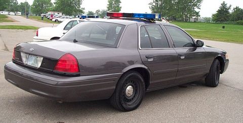 2001 Ford Crown Victoria - This police car, a 2001 Ford Crown Victoria, is parked outside on a cloudy day with another vehicle behind it.