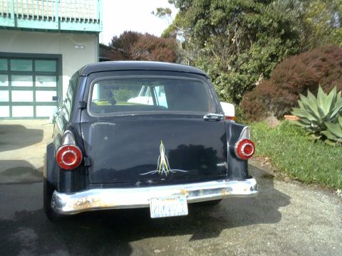 1972 Ford Ranchero - The rear view of a dark colored classic car, possibly a station wagon or sedan, is shown parked in a driveway. The car has a chrome bumper,…