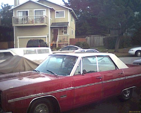 1972 Ford Ranchero - A red 1970s era sedan with a white vinyl top is parked in front of a house with a garage. A white van is parked behind the sedan.