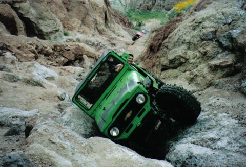 1993 Ford Bronco - A green off-road vehicle navigates a steep, rocky incline, with another vehicle visible further up the trail.