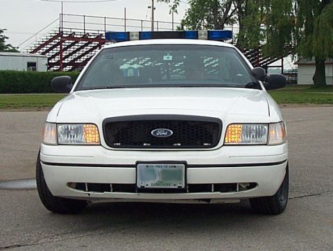 2001 Ford Crown Victoria - A white 2001 Ford Crown Victoria police car is parked facing the camera, with bleachers in the background.