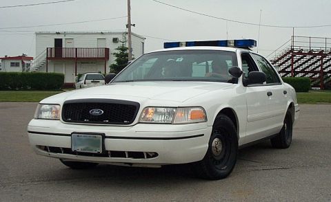 2001 Ford Crown Victoria - White police car with light bar on the roof, parked outdoors.