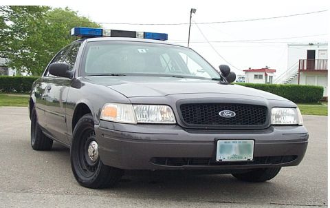 2001 Ford Crown Victoria - Gray Ford Crown Victoria Police Interceptor with roof light bar and Ford grille badge, parked front-three-quarter view.