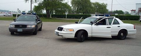 2001 Ford Crown Victoria - Two Ford Crown Victoria police cars are parked on asphalt, with the white car's doors open.