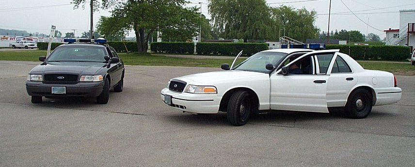 Two Ford Crown Victoria police cars, one black and one white with doors open