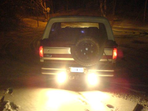 1989 Ford Bronco - The rear of a 1989 Ford Bronco is illuminated by its backup lights in a snowy, dark setting.