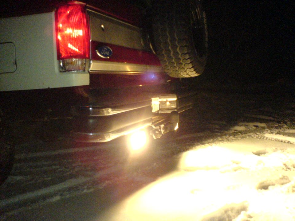 1989 Ford Bronco rear bumper with trailer hitch and taillight illuminated at night