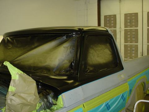 1979 Ford Bronco - A vehicle's cab is covered in masking and plastic sheeting, ready for a paint job in a workshop.