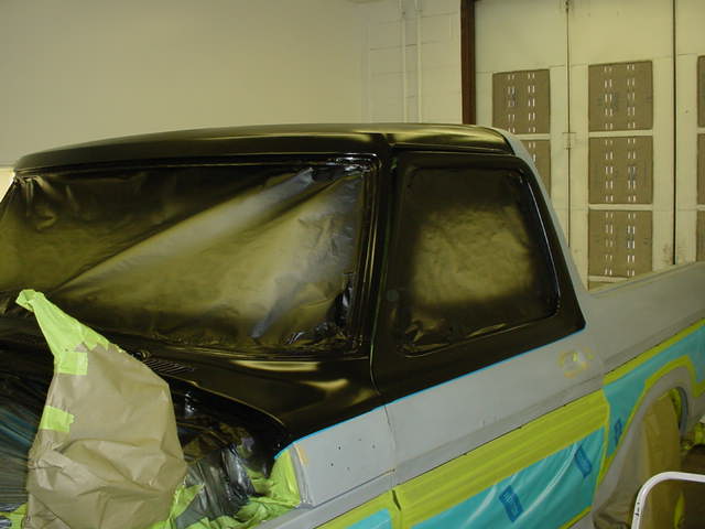 Truck cab with windows taped off, being prepped for paint. Body is gray, with black trim and some blue masking tape